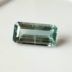 Puede incluir: Una piedra preciosa de aguamarina azul claro con un corte rectangular esmeralda.