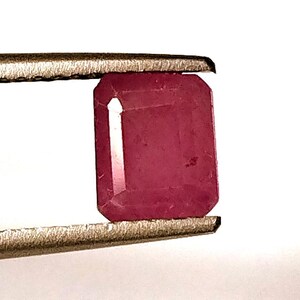 Puede incluir: Una piedra preciosa de color rojo oscuro tallada en esmeralda, sostenida por unas pinzas.