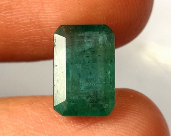 May include: A deep green emerald gemstone cut into a rectangular shape.