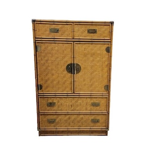 May include: A tall, light brown bamboo cabinet with two upper drawers, two cabinet doors, and two lower drawers. The cabinet has brass hardware and corner accents. The woven bamboo design gives it a natural, textured look.