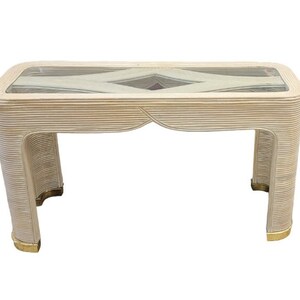 May include: Rectangular coffee table with a glass top and a light beige, ribbed frame. The table has a decorative diamond pattern on the glass and gold accents on the legs. A stylish piece of furniture for a living room.