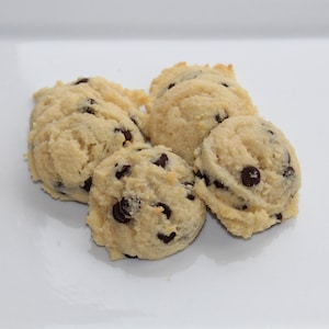 May include: Five soft, light brown, chocolate chip cookies on a white surface.