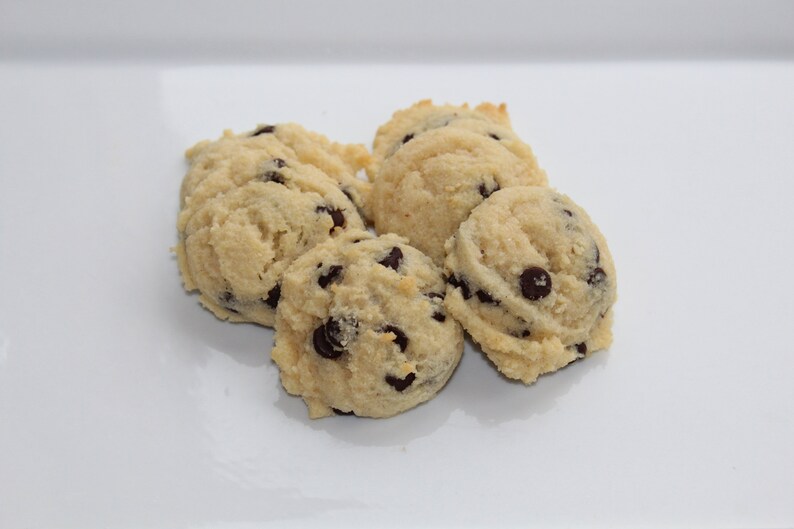 May include: Five soft, light brown, chocolate chip cookies on a white surface.