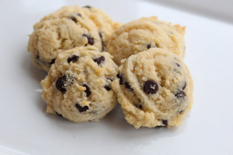 May include: Four soft, light brown cookies with chocolate chips on a white surface.