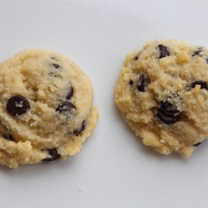 May include: Two light brown chocolate chip cookies on a white surface. The cookies are slightly misshapen and have a few chocolate chips visible.