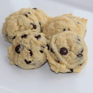 May include: Close-up of four soft, golden brown chocolate chip cookies on a white surface.