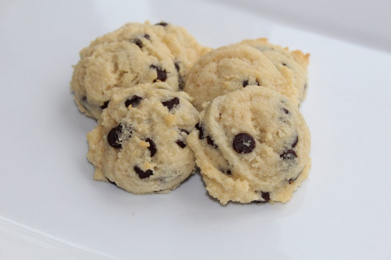May include: Close-up of four soft, golden brown chocolate chip cookies on a white surface.