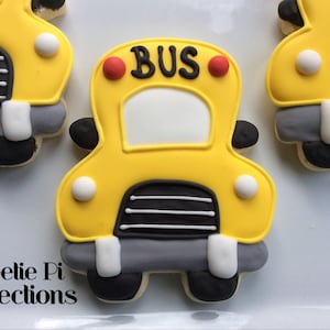 May include: Yellow bus-shaped cookie decorated with black and white stripes, red circles, and the word "BUS" in black lettering.