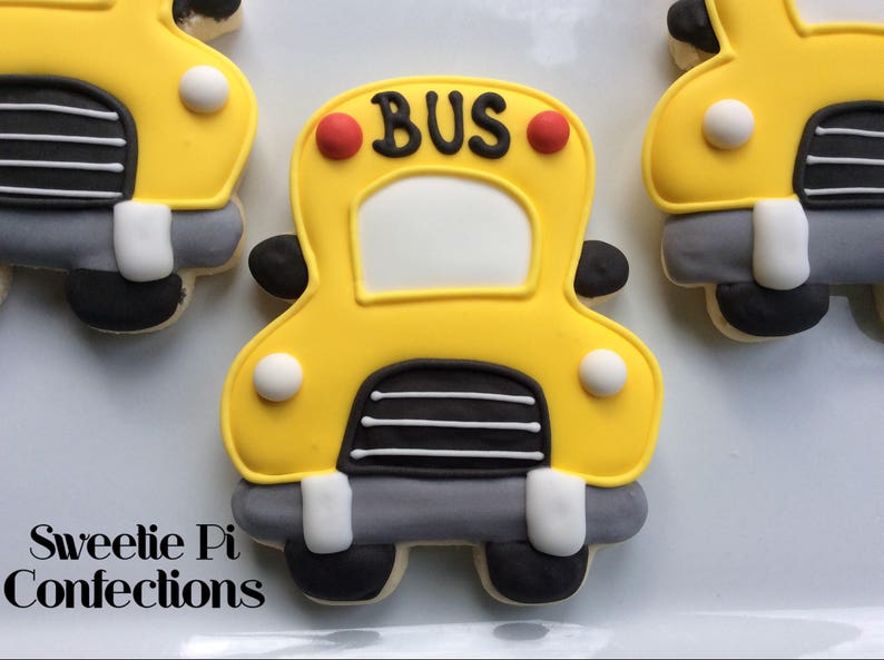 May include: Yellow bus-shaped cookie decorated with black and white stripes, red circles, and the word "BUS" in black lettering.