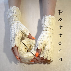 Puede incluir: Un par de guantes sin dedos de color blanco hechos a crochet con un borde festoneado. Los guantes están siendo sostenidos por una persona con esmalte de uñas naranja. También se puede ver una madeja de hilo blanco y un ganchillo.