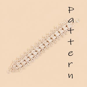 Può includere: Un braccialetto all'uncinetto beige con un motivo ripetitivo a punto puff testurizzato, bordi smerlati e una chiusura a moschettone color argento. La parola Pattern è scritta verticalmente in nero a destra del braccialetto.