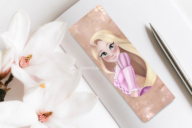 Op de afbeelding: Een bladwijzer met een cartoonillustratie van Rapunzel uit de Disney-film Tangled. Ze heeft lang blond haar, een roze jurk en een kroon. De achtergrond is lichtbruin met een bloemmotief.