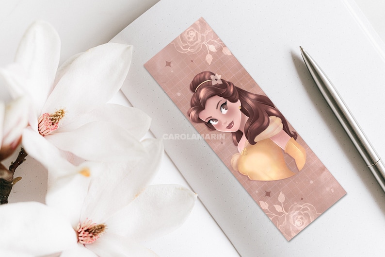 Op de afbeelding: Een roze en gouden bladwijzer met een cartoonillustratie van Belle uit Disney's Belle en het Beest. De bladwijzer heeft een subtiel rasterpatroon en een bloemmotief.