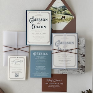 Full Emerson western wedding invitation suite featuring dusty blue, ivory and warm brown stationery with a scenic ranch envelope liner and layered translucent details.