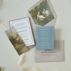 Romantic dusty blue and green wedding stationery featuring a bordered ivory invitation, scenic landscape vellum wrap and coordinating envelope with elegant swan artwork.