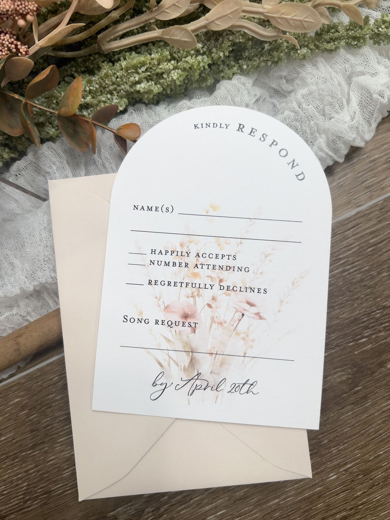 May include: A white RSVP card with a floral design and the text "KINDLY RESPOND" in a curved arch. The card has fields for the guest's name, RSVP options, and a song request. The text "by April 20th" is written in cursive at the bottom of the card.