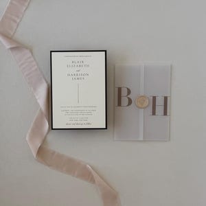 Ivory wedding invitation layered with translucent monogram vellum and paired with a warm brown details card, styled with soft blush ribbon on a neutral background.