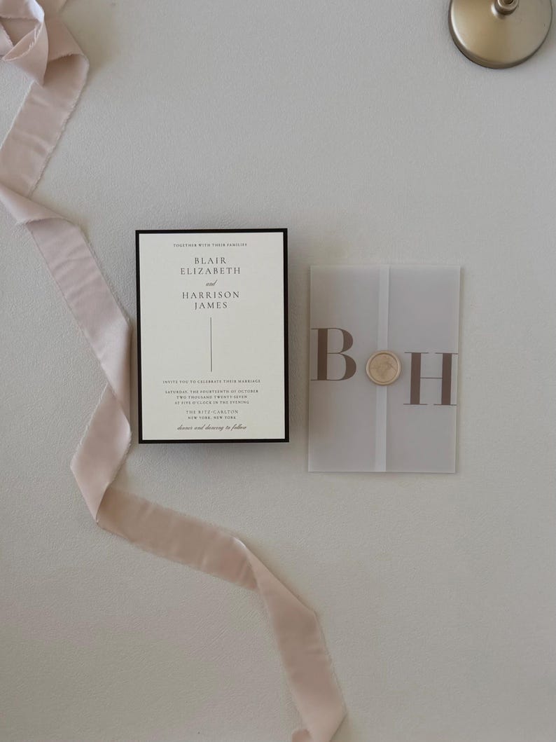 Ivory wedding invitation layered with translucent monogram vellum and paired with a warm brown details card, styled with soft blush ribbon on a neutral background.