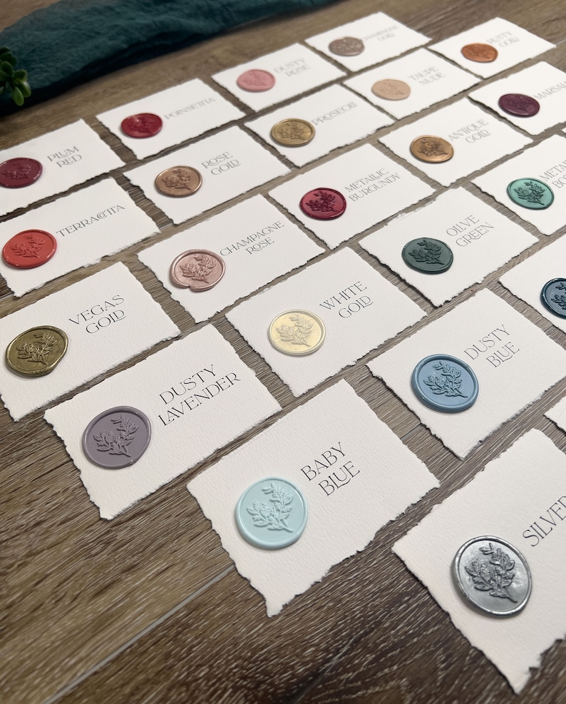 May include: A collection of rectangular white cards with deckled edges, each featuring a circular wax seal with a floral design. The cards are labeled with color names including Plum Red, Poinsettia, Rose Gold, Champagne Rose, Vegas Gold, Dusty Lavender, White Gold, Dusty Blue, Baby Blue, and Silver.