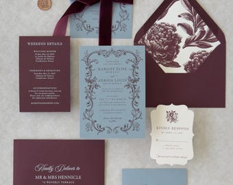 May include: A wedding invitation suite featuring dusty blue cards with ornate dark burgundy borders and text, paired with deep burgundy envelopes, a matching RSVP card, and a dark burgundy velvet ribbon tied around the main invitation card.