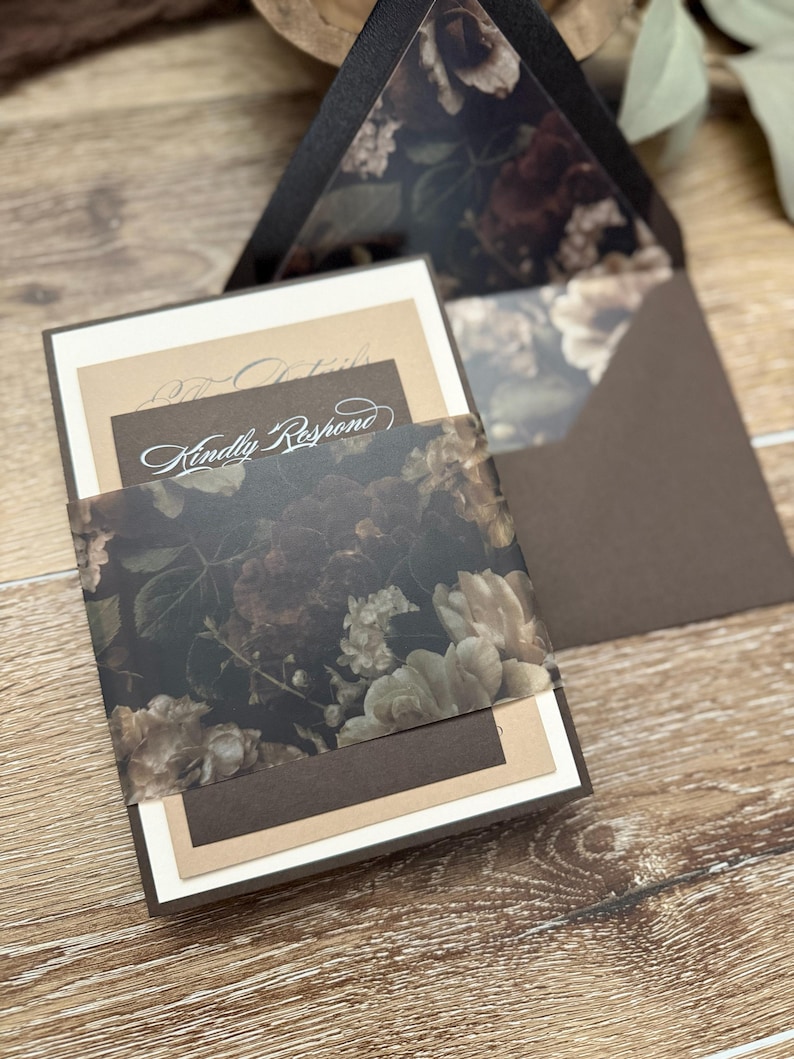 May include: A wedding invitation suite featuring a dark brown envelope with a floral patterned liner, a cream-colored card, a tan card, and a dark brown RSVP card with the text Kindly Respond, all held together by a translucent floral belly band.