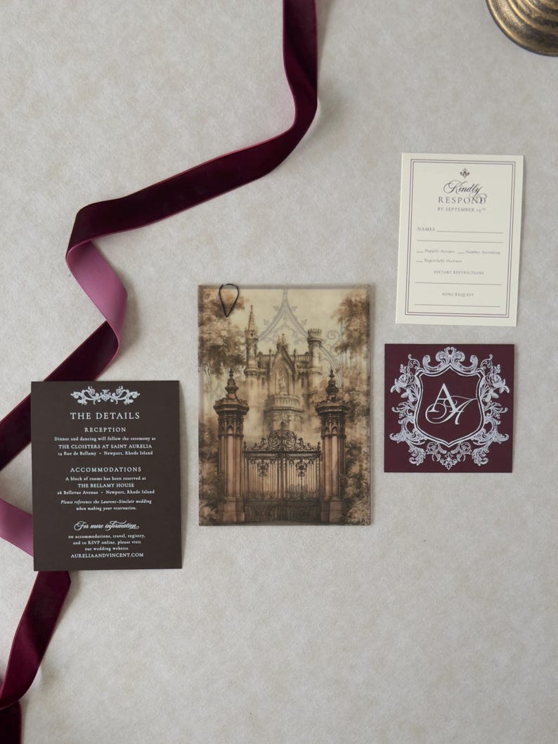 Aurelia wedding invitation accessories featuring dramatic sepia castle-gate vellum, dark Bitter Chocolate details card, ivory traditional RSVP, and ornate Claret crest tag arranged with burgundy velvet ribbon.