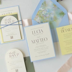 Romantic pastel wedding invitation suite featuring a pale blue layered invitation, butter yellow details card, ivory arch RSVP card and coordinating blue floral-lined envelope.