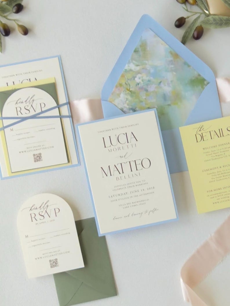 Romantic pastel wedding invitation suite featuring a pale blue layered invitation, butter yellow details card, ivory arch RSVP card and coordinating blue floral-lined envelope.