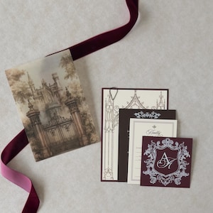 Vintage castle wedding invitation suite with printed Gothic gate vellum overlay, cream invitation, black teardrop paperclip, burgundy Claret crest tag, and coordinating dark chocolate and ivory stationery.