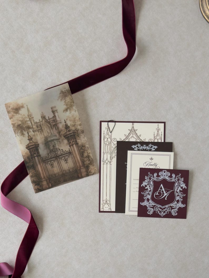 Vintage castle wedding invitation suite with printed Gothic gate vellum overlay, cream invitation, black teardrop paperclip, burgundy Claret crest tag, and coordinating dark chocolate and ivory stationery.