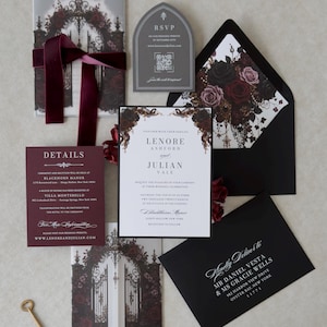 Lenore Gothic floral wedding invitation suite featuring a white invitation with Ebony backing mat, Claret burgundy details card, Dark Grey tombstone-shaped online RSVP, and printed vellum jacket with Gothic gates and dark roses. Styled with an Ebony envelope, coordinating floral liner, and burgundy velvet ribbon.