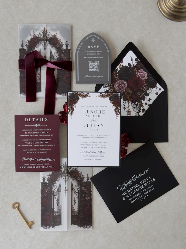 Lenore Gothic floral wedding invitation suite featuring a white invitation with Ebony backing mat, Claret burgundy details card, Dark Grey tombstone-shaped online RSVP, and printed vellum jacket with Gothic gates and dark roses. Styled with an Ebony envelope, coordinating floral liner, and burgundy velvet ribbon.