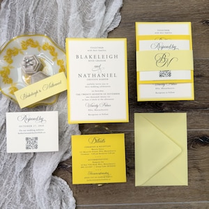 May include: Wedding invitation suite with yellow and white stationery. Includes invitation cards, RSVP cards, details card, and an envelope. The invitation features the names Blakeleigh and Nathaniel. A small plate with a ring box is also present.