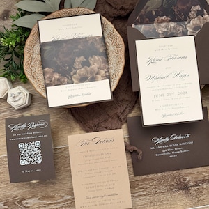 May include: A wedding invitation suite featuring cream-colored cards with dark brown text, a dark floral envelope liner, and a matching belly band. Includes a QR code response card, a details card, and an addressed envelope with dark brown accents.