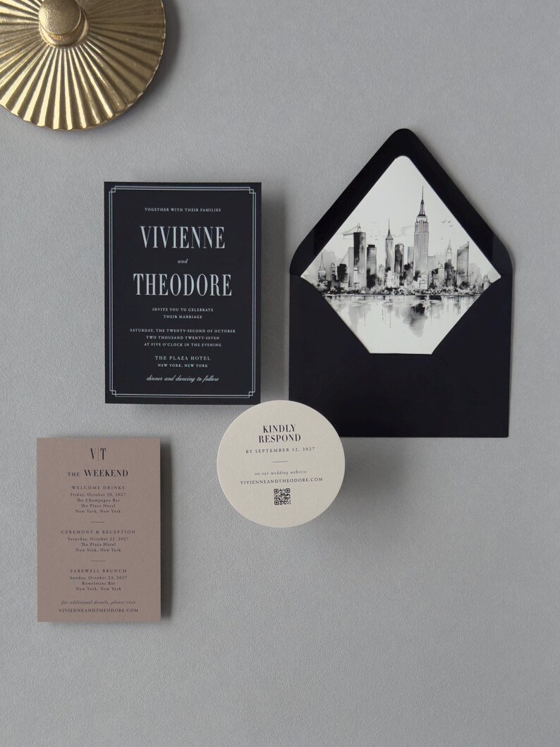 Black Vivienne wedding invitation suite with taupe details card, ivory round RSVP card and coordinating skyline-lined envelope styled on a neutral background.
