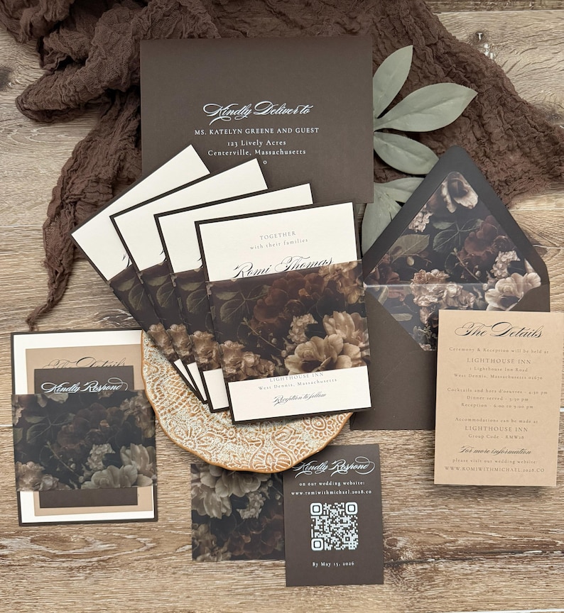 May include: A wedding invitation suite featuring dark brown envelopes, cream-colored cards, and belly bands with a dark floral print. The set includes a mailing envelope addressed to Ms. Katelyn Greene, a details card, and a response card with a QR code.