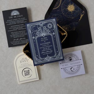 Elara celestial wedding invitation suite featuring a navy blue invitation with intricate silver Art Deco sun, moon, and star illustrations, black details card, ivory arch RSVP card, lavender celestial tag, and black A7 envelope with gold astronomical chart liner.
