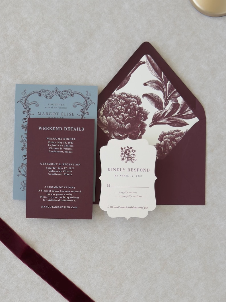 Ivory scalloped RSVP card with burgundy typography paired with dusty blue RSVP envelope and coordinating wedding stationery