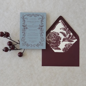 Dusty blue wedding invitation displayed with burgundy A7 envelope and vintage botanical floral envelope liner