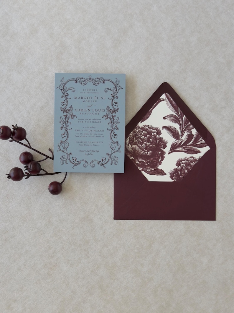Dusty blue wedding invitation displayed with burgundy A7 envelope and vintage botanical floral envelope liner