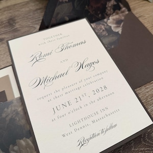 May include: A cream-colored wedding invitation card with dark brown text and borders. The text reads: Together with their families Romi Thomas and Michael Hayes request the pleasure of your company at their marriage celebration June 21st, 2028.