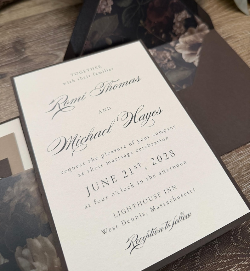May include: A cream-colored wedding invitation card with dark brown text and borders. The text reads: Together with their families Romi Thomas and Michael Hayes request the pleasure of your company at their marriage celebration June 21st, 2028.