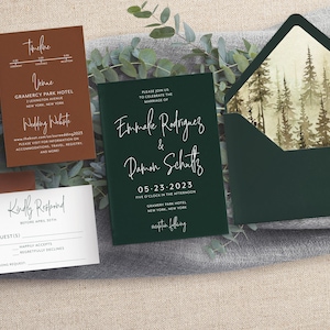 May include: A set of wedding invitations with a forest theme. The invitations are printed on dark green and brown cardstock with white calligraphy. The envelope is dark green with a watercolor illustration of a forest.