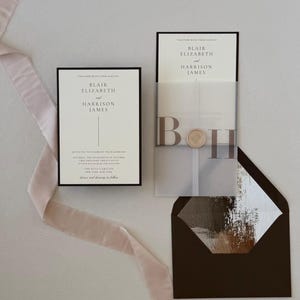 Elegant Blair wedding invitation displayed with translucent monogram vellum, soft blush ribbon and a brown envelope opened to reveal a romantic floral liner.
