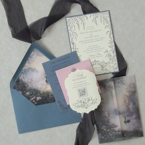 Romantic swan lake wedding stationery with an open Marina blue envelope revealing a dreamy woodland water scene, an ivory botanical invitation, scalloped RSVP card, pink tag, and illustrated vellum jacket.