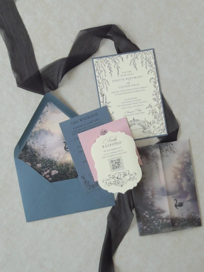 Romantic swan lake wedding stationery with an open Marina blue envelope revealing a dreamy woodland water scene, an ivory botanical invitation, scalloped RSVP card, pink tag, and illustrated vellum jacket.