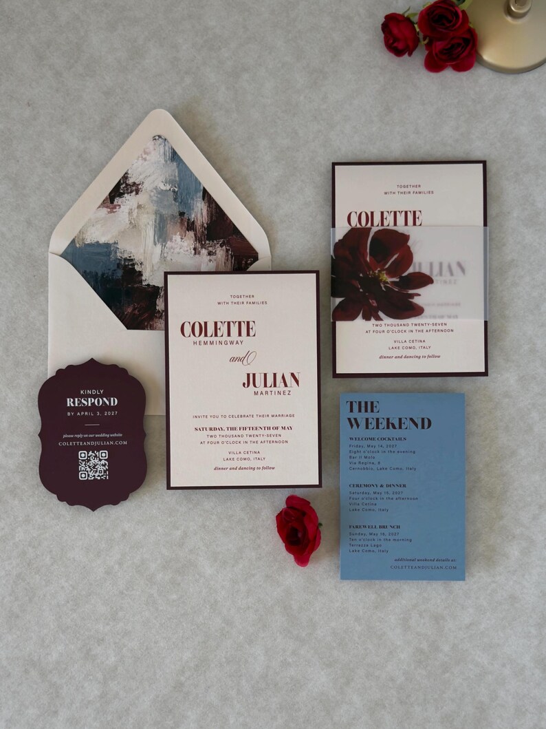 Burgundy and dusty blue floral wedding invitation suite featuring an ivory invitation with dark floral artwork, dusty blue details card, burgundy scalloped RSVP card, and burgundy mailing envelope with coordinating floral liner.