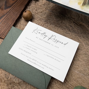May include: A white RSVP card with black text. The card has a section for the guest's name, a checkbox for happily accepts, a checkbox for regretfully declines, a space for the number attending, and a space for a song request. The card also includes the text "Kindly Respond by September 10, 2024" and "Guests may also RSVP on our wedding website: PadmaandHarrison.com".