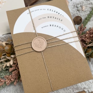 May include: A brown invitation card with a white and pink layered design. The card is tied with twine and sealed with a wax stamp. The text on the card reads "Please join us to celebrate... all the details... kindly respond".