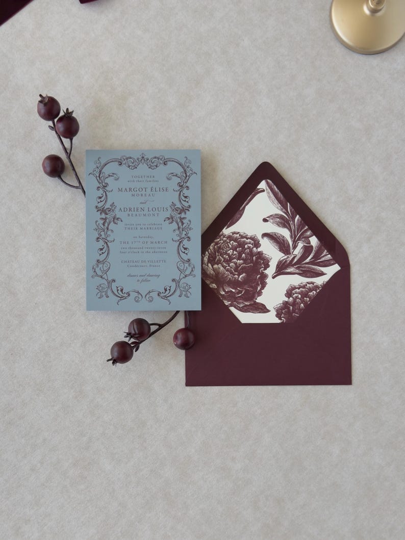 Dusty blue wedding invitation displayed with burgundy A7 envelope and vintage botanical floral envelope liner